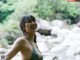 A woman in a green bikini standing in front of a river.