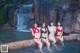 A group of women in bikinis posing in front of a waterfall.