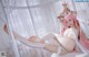 A woman with pink hair is sitting on a bed.